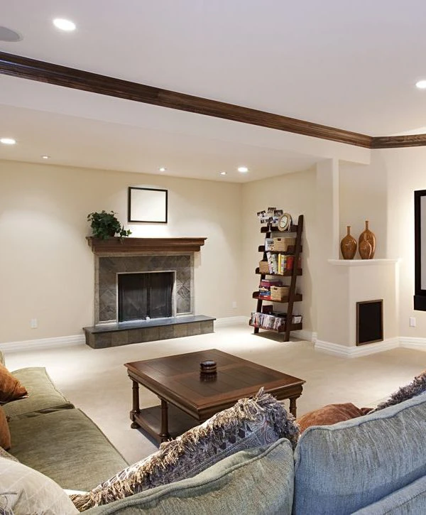 A beautifully finished basement in Auburn, MA, featuring a cozy tile fireplace with a wood mantle, ladder shelving, and plush carpeting installed by remodeling contractors.