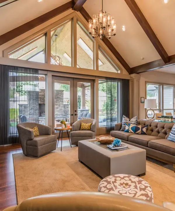 A luxury open-concept living room featuring vaulted ceilings with dark wood beams and floor-to-ceiling windows, showcasing work by design-build remodeling companies in Auburn, MA.