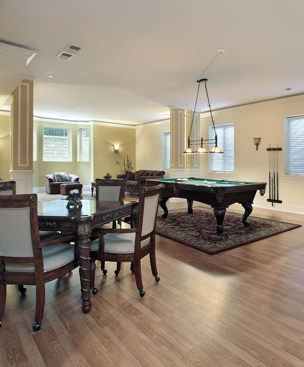 Spacious finished basement featuring a classic wooden dining table, a pool table on a decorative rug, and a cozy seating area, completed by basement remodeling contractors in Worcester, MA.