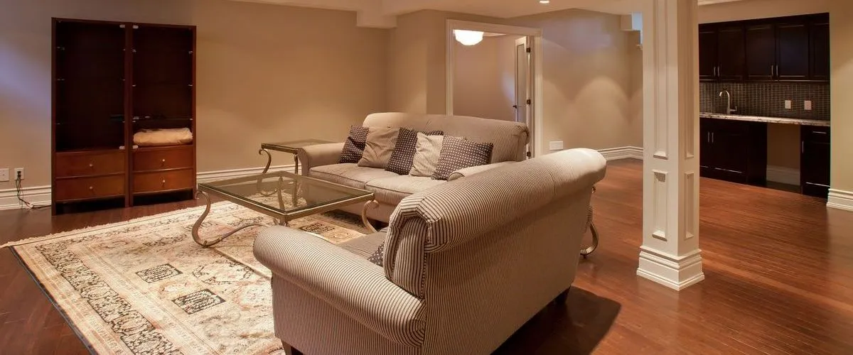 Spacious finished basement featuring dark hardwood floors, a white decorative pillar, and a functional wet bar with dark cabinetry in the background.