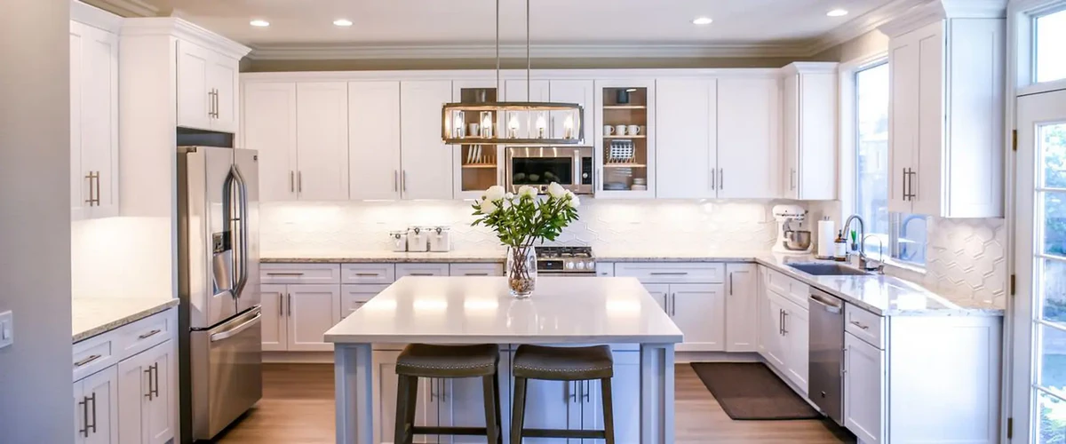 Bright and spacious modern white kitchen showcasing a central island, stainless steel appliances, a geometric tile backsplash, and elegant glass lighting.