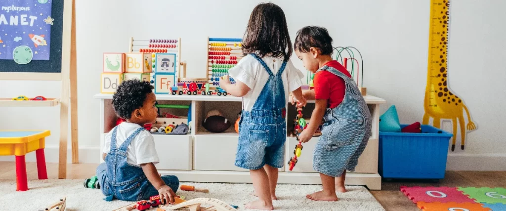 Two young toddlers actively playing with wooden trains and an abacus in a bright, colorful basement kids playroom equipped with toy storage.