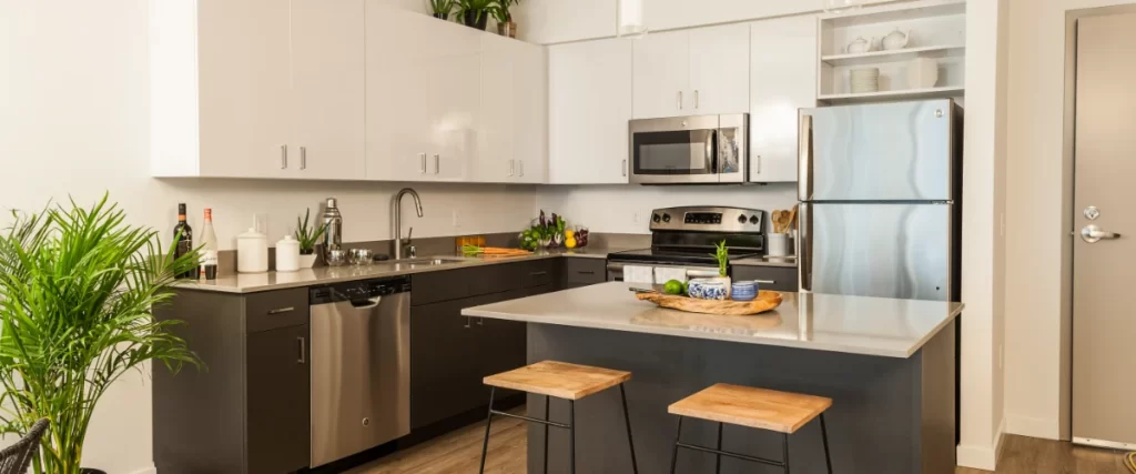 A clean, modern two-tone kitchen featuring dark grey base cabinets, white upper cabinets, and a compact island with wooden stools.
